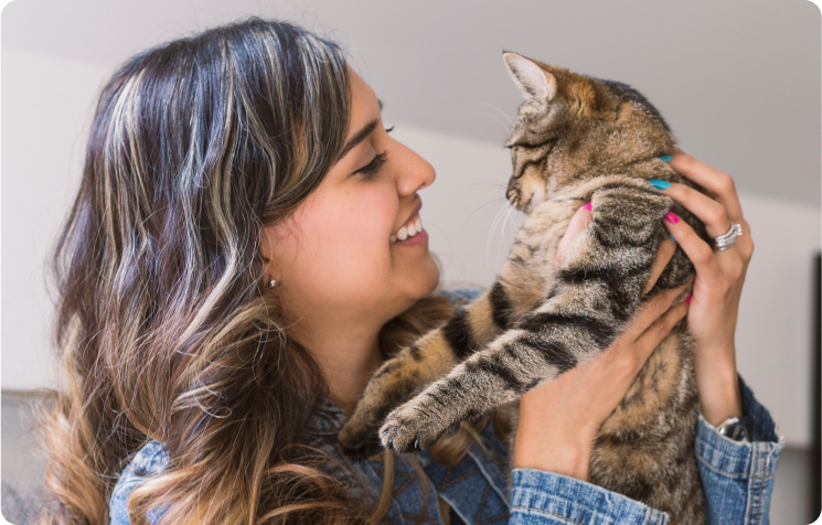 A woman smiling and holding a tabby cat, looking at each other affectionately.